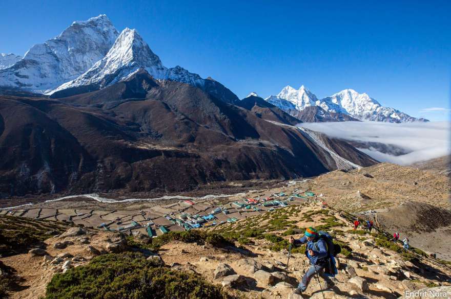 Trekker hiking above Dingboche village with stunning views of Ama Dablam and Himalayan mountains on the Everest Base Camp trail.